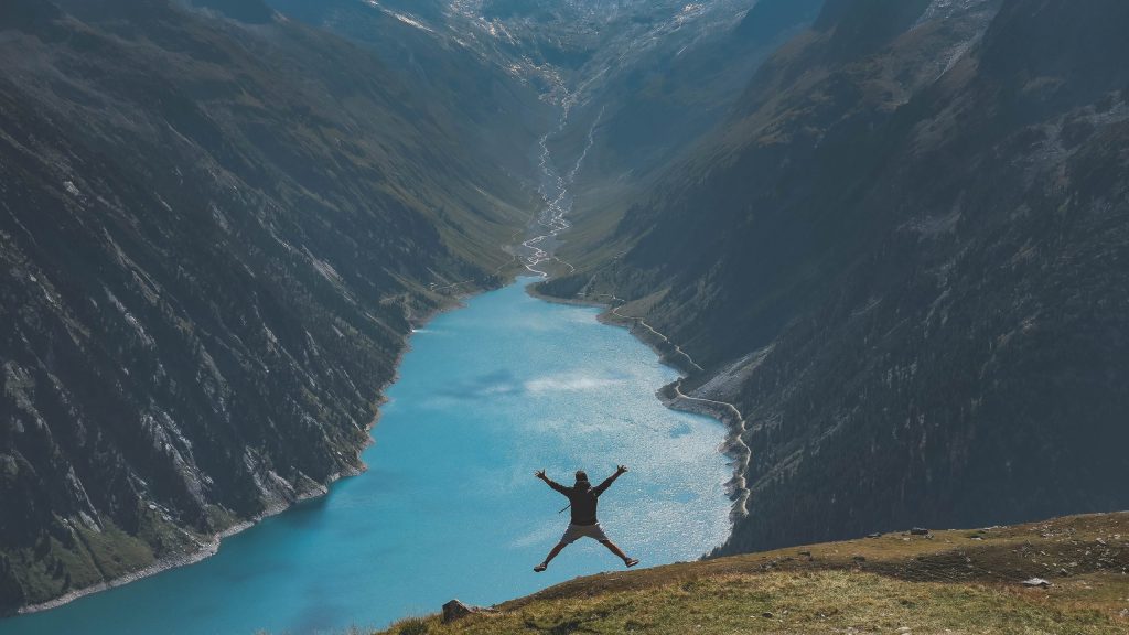 man jumping in front of mountains and a lake